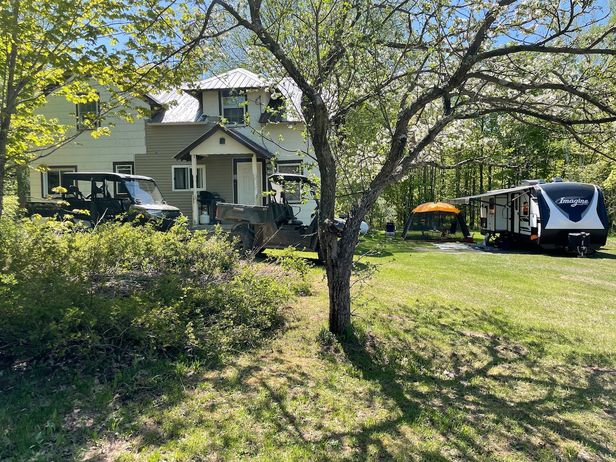 Yooper Lodge in spring or summer with green wooded grounds, trailer space, and outdoor equipment