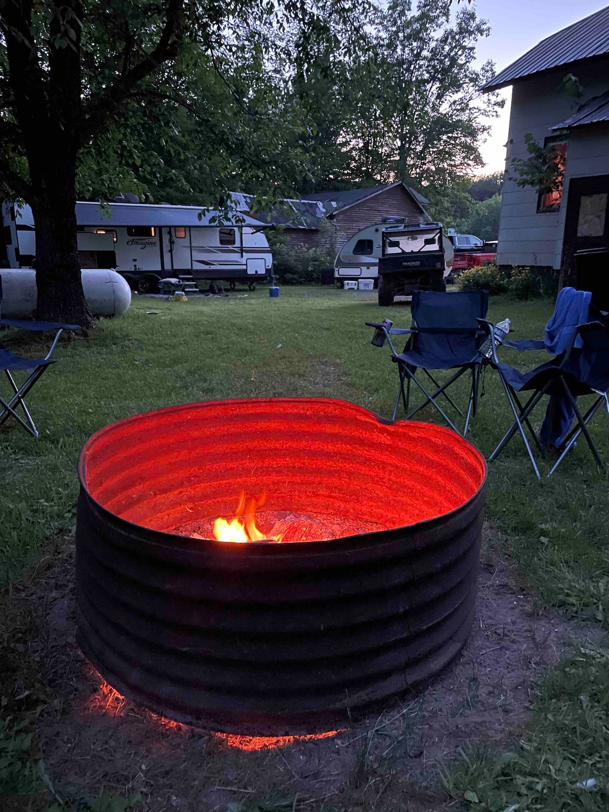 Outdoor fire ring at Yooper Lodge with chairs, lawn, campers, and trees